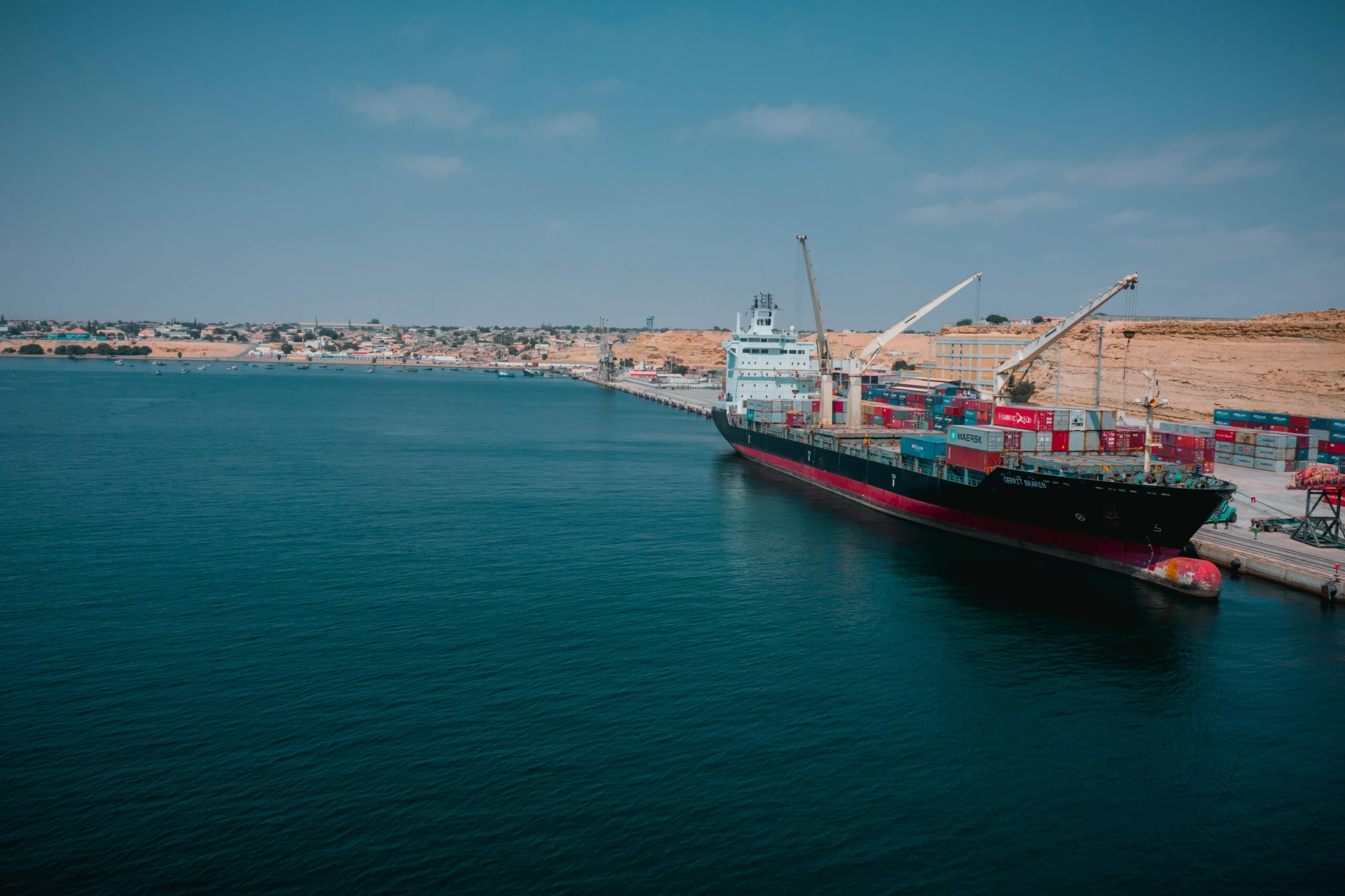 Services Cargo ship docked at Namibe port in Angola with shipping containers and cranes.